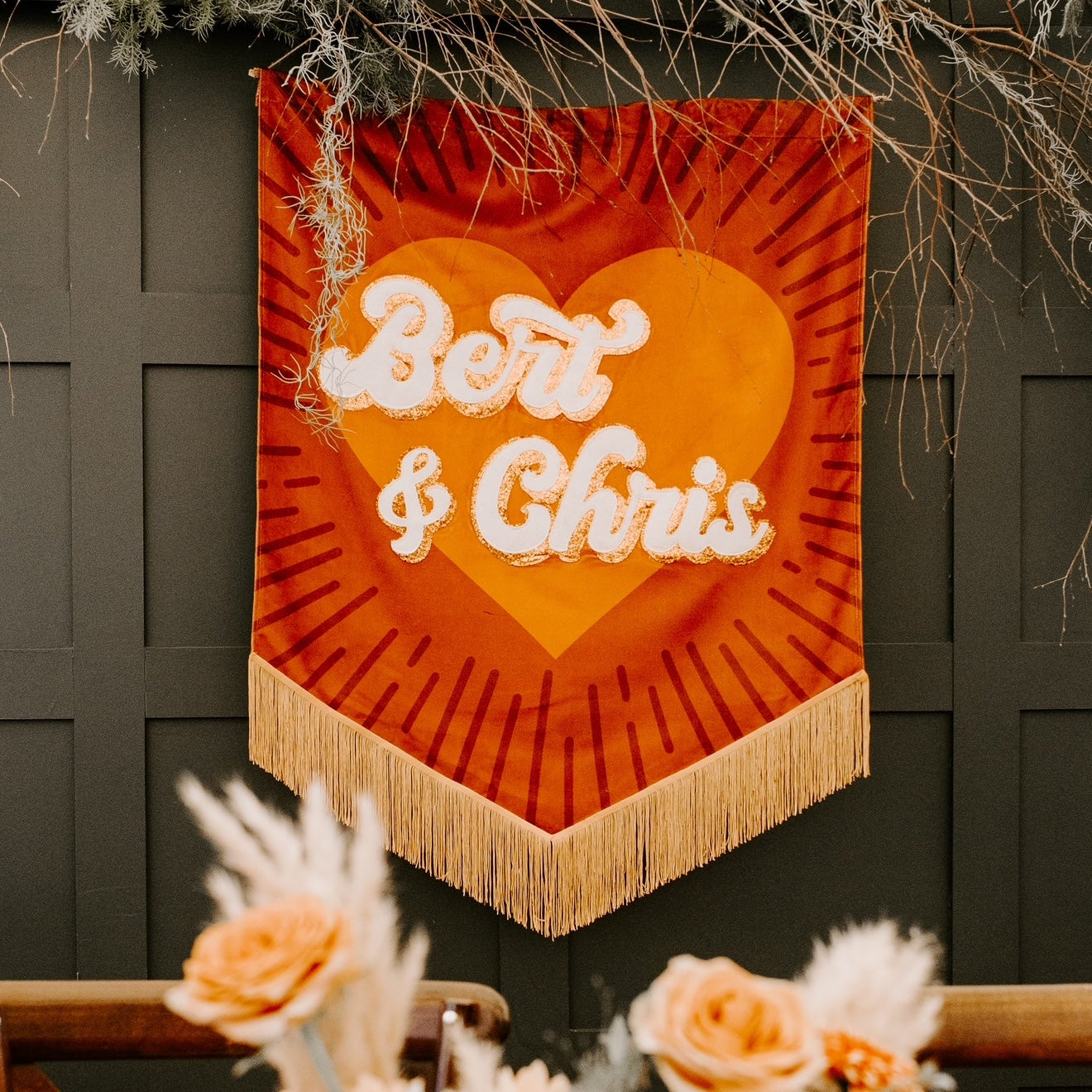 Decorative wall hanging with 'Bert & Chris' text above a floral arrangement.